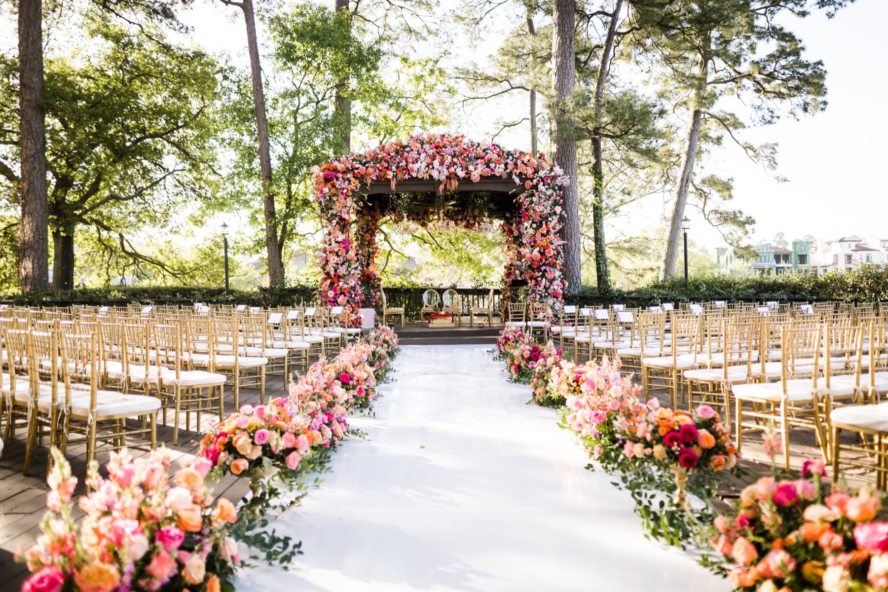 Ceremony venue with ghost chairs reflected in mirror aisle floor beneath floral archway