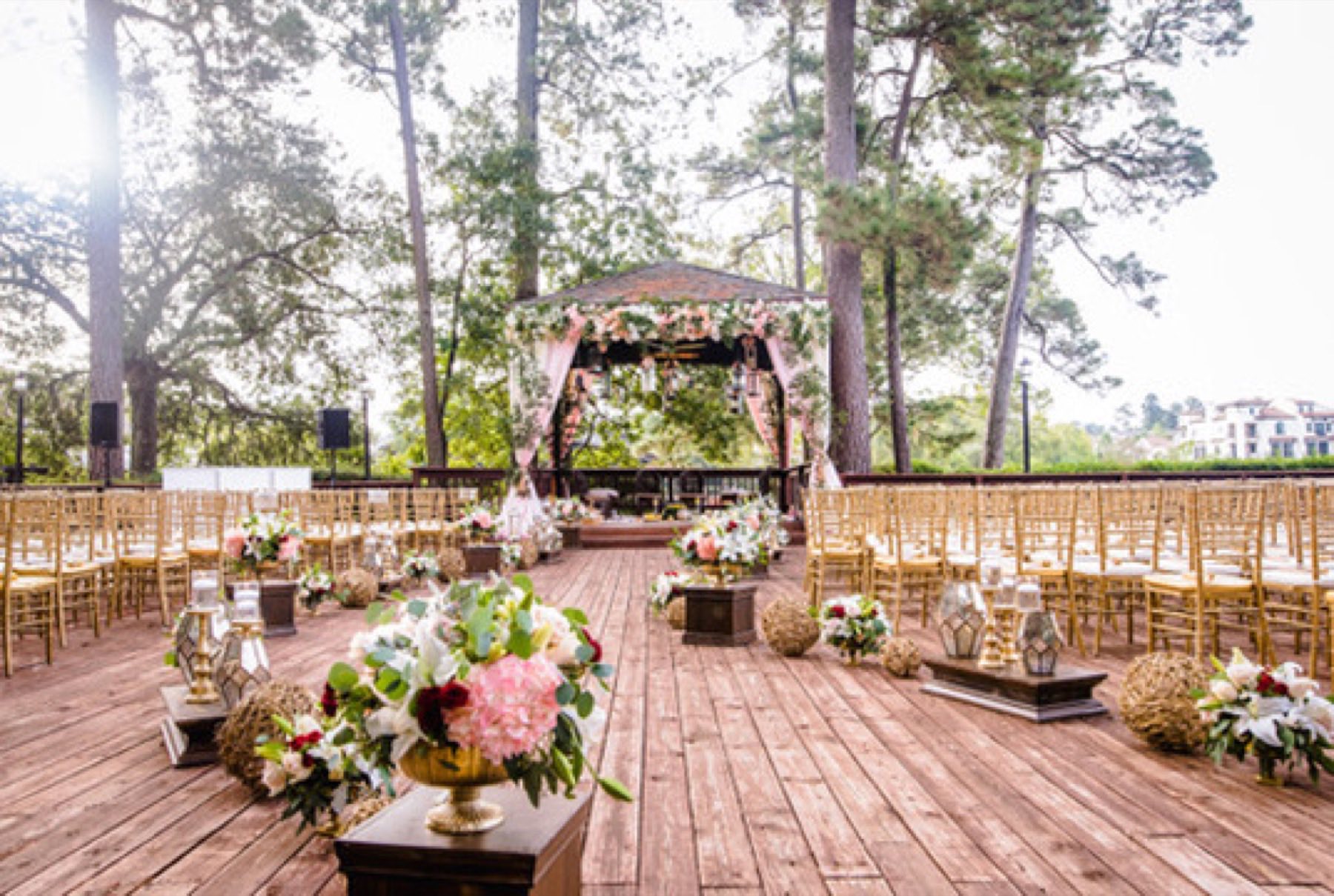 Ceremony set on a wooden deck among tall trees with floral mandap and lantern accents