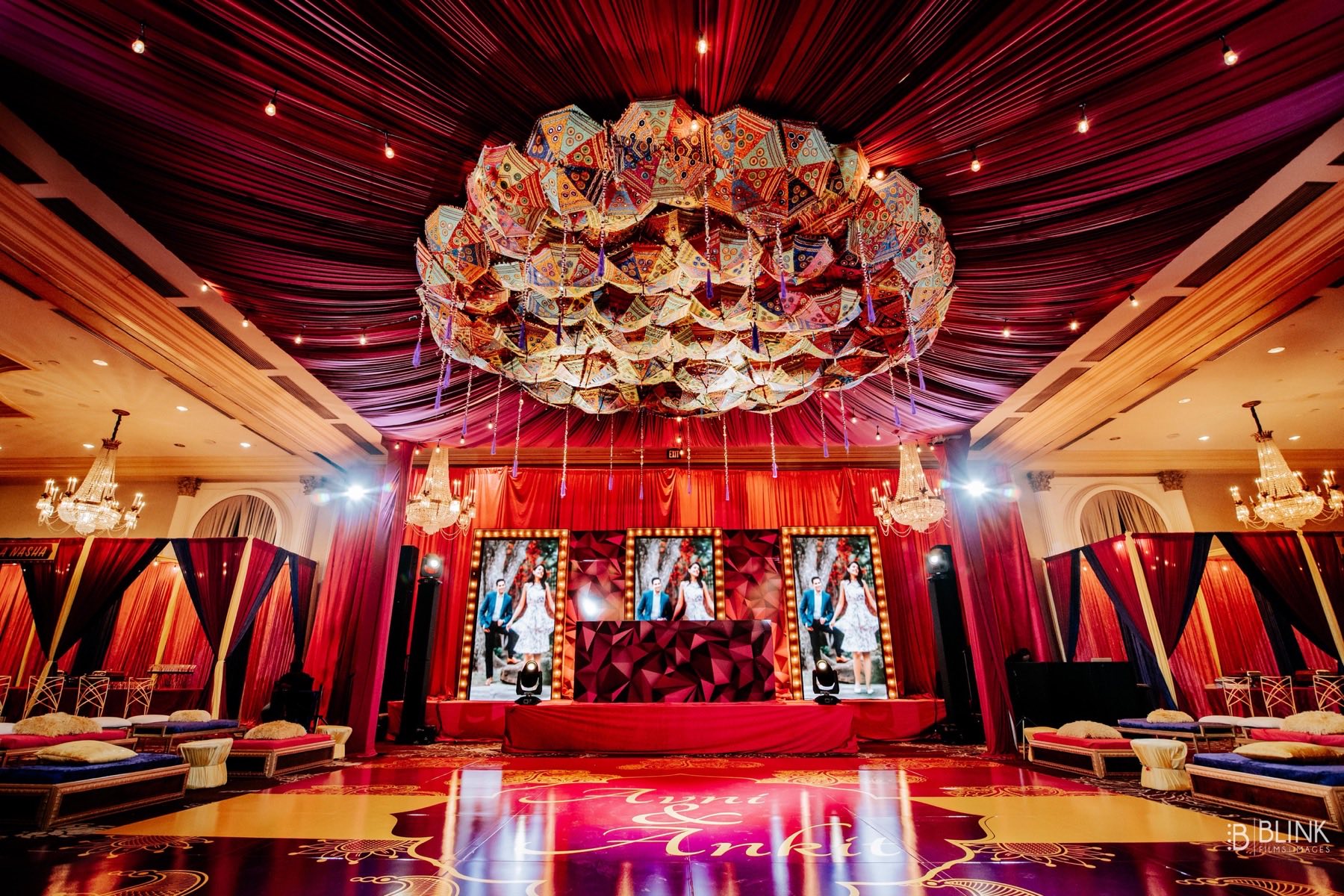 Dramatic sangeet stage with hanging umbrella ceiling installation and red draping