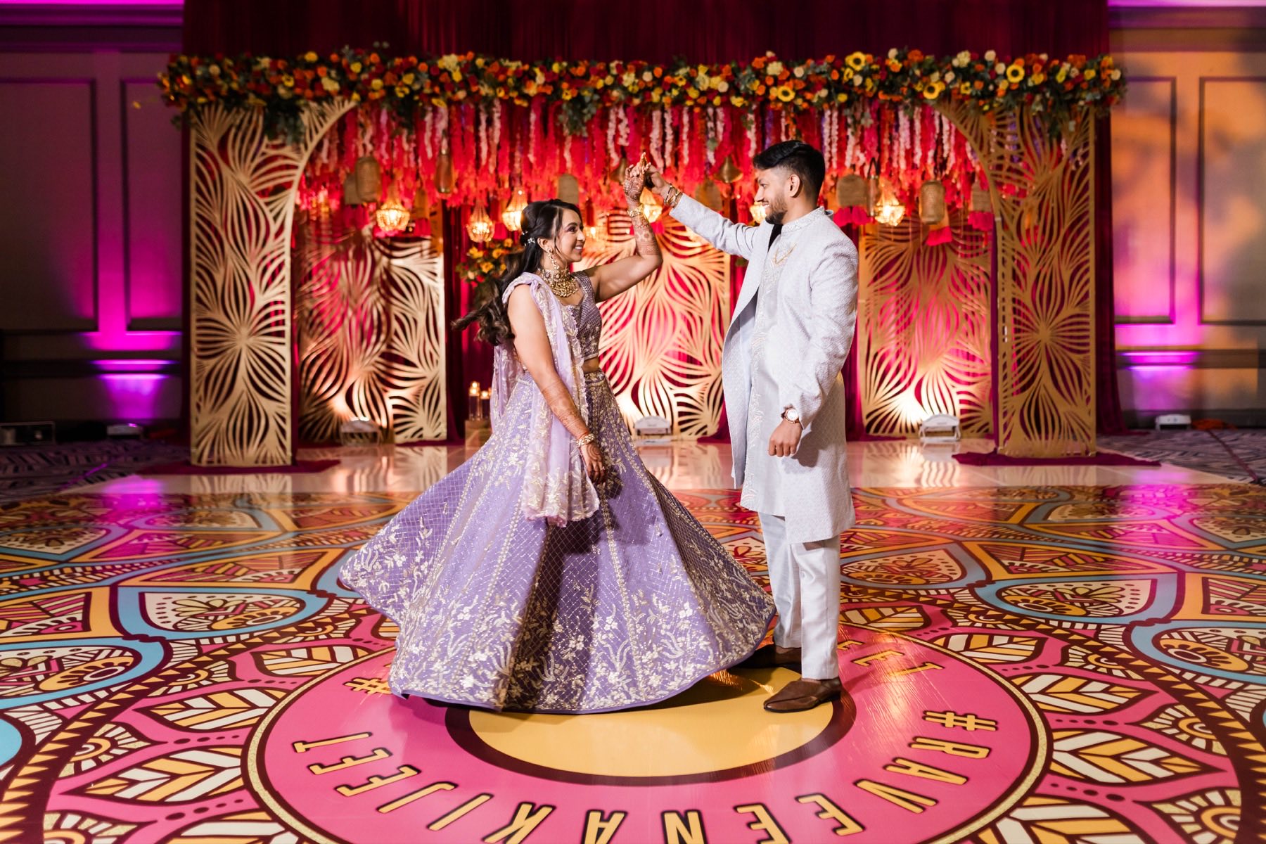 Couple dancing on vibrant patterned mandala floor at sangeet, bride in lilac lehenga