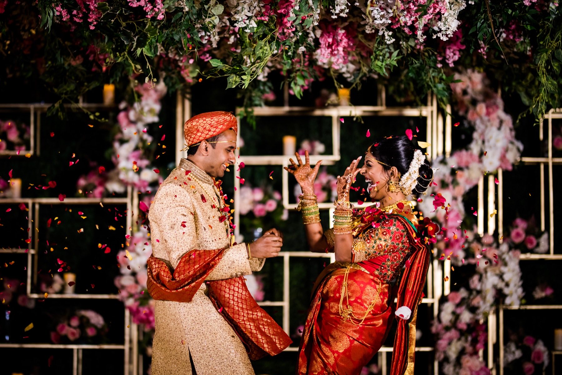 Couple laughing and tossing flowers at each other at ceremony floral backdrop